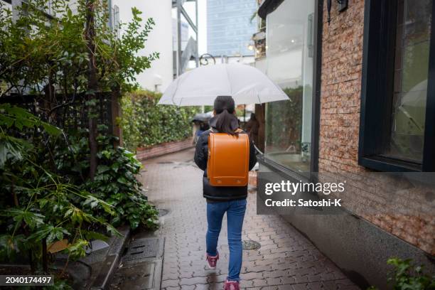 rear view of japanese elementary school student girl carrying a ‘randoseru’ school bag in a rainy day - harajuku girls stock pictures, royalty-free photos & images