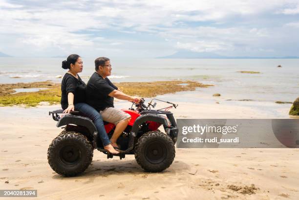 mature couple riding a quad atv down the beach - driving barefoot stock pictures, royalty-free photos & images