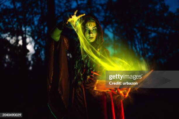 evil witch practicing magic using a magic book in the forest at night - horror story stock pictures, royalty-free photos & images