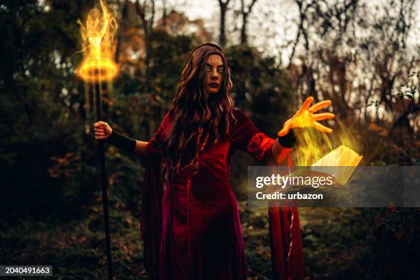 evil witch practicing magic in the forest using a magic cane and a book at night - wicca stock pictures, royalty-free photos & images