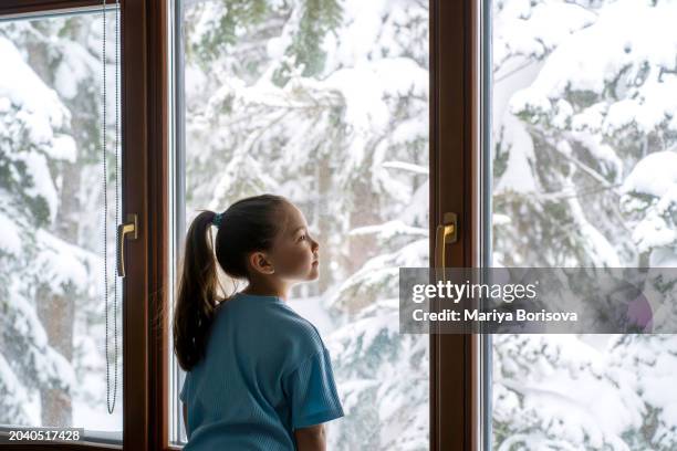 a girl in a blue suit stands against the backdrop of a large window with a winter landscape. - house golden hour stock pictures, royalty-free photos & images