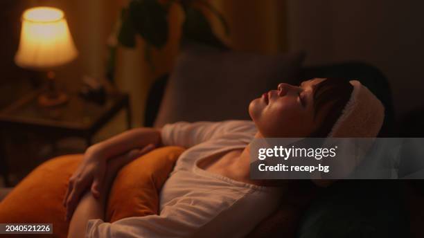 frau ruht sich nachts zu hause auf dem sofa aus - warmes licht stock-fotos und bilder