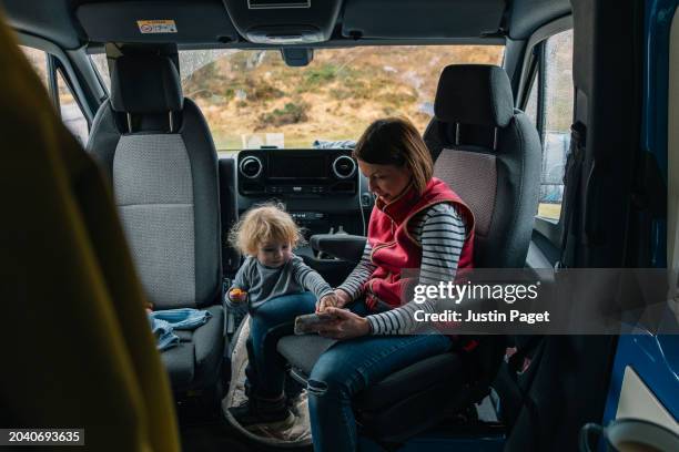 a mature woman watches a tv show on her smartphone with her toddler daughter as they relax in their campervan - thier stock pictures, royalty-free photos & images