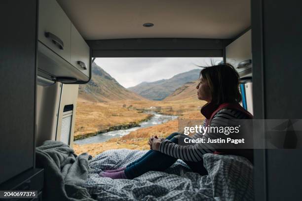 view of a mature woman taking in the stunning vista of the glen etive valley and mountains from the rear of her campervan - camping selvagem imagens e fotografias de stock