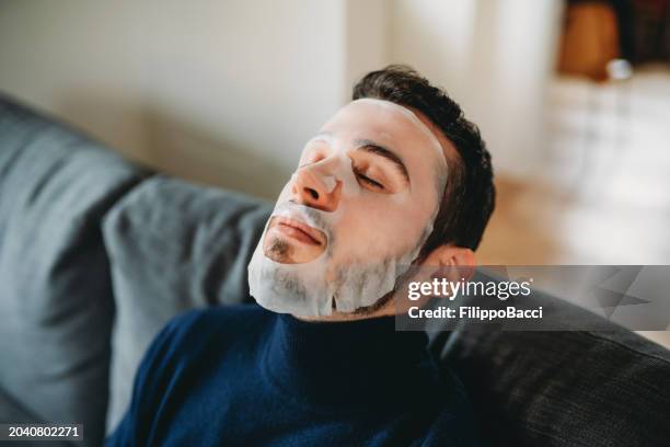 a young adult man is wearing a fabric face mask during his daily beauty routine - cloth face mask stock pictures, royalty-free photos & images