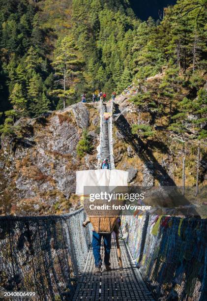 nepal porter carring heavy loaded basket across rope bridge himalayas - nepal culture stock pictures, royalty-free photos & images