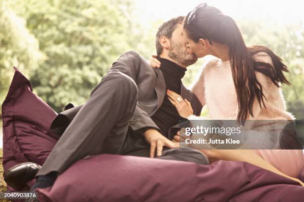 couple sitting on large cushion in park kissing - big hug picture stock pictures, royalty-free photos & images