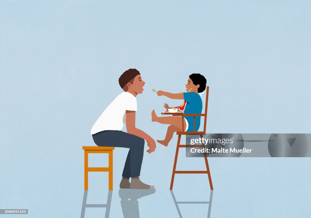 Baby son in high chair feeding father