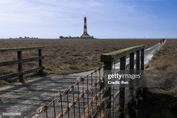 travel destination: bridge to westerhever lighthouse (schleswig-holstein, germany) - westerhever vuurtoren stockfoto's en -beelden