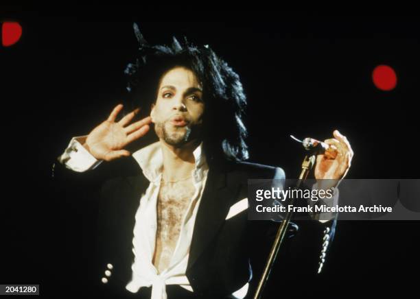 American singer and songwriter Prince stands on stage with a microphone, one hand by his ear to hear the crowd response, during a concert, February...