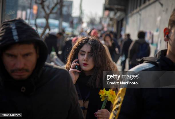 Young Iranian woman is walking along a sidewalk on Enghelab Avenue in downtown Tehran, Iran, on February 29 carrying flowers and not wearing a...