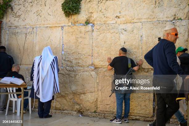 Person carrying a rifle prays at the Western Wall on February 26, 2024 in Jerusalem. Frustrations with the government have grown as over 100 hostages...