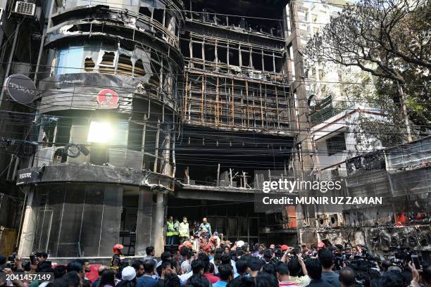 People gather near a commercial building a day after a fire accident, as firefighters and forensic expert inspect the site in Dhaka on March 1, 2024....