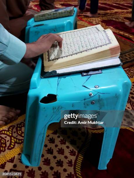 close up of a human hand reading koran (quran) in a mosque on a cracked koran support or rail. - trust god stock pictures, royalty-free photos & images