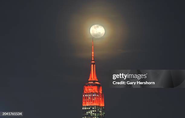Percent illuminated wanning gibbous moon rises through clouds behind the Empire State Building in New York City, lit in red to mark the 25th...