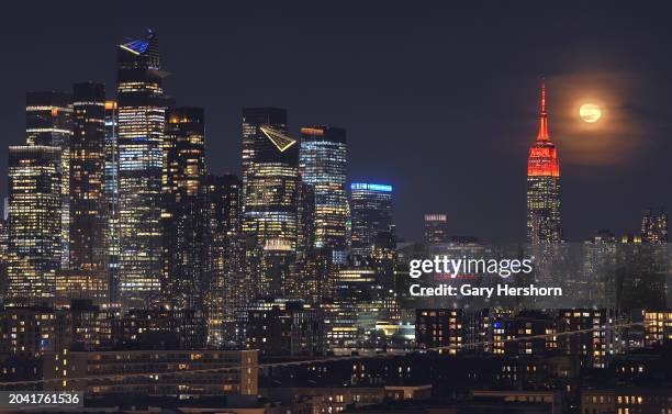 Percent illuminated wanning gibbous moon rises through clouds behind the Empire State Building in New York City, lit in red to mark the 25th...