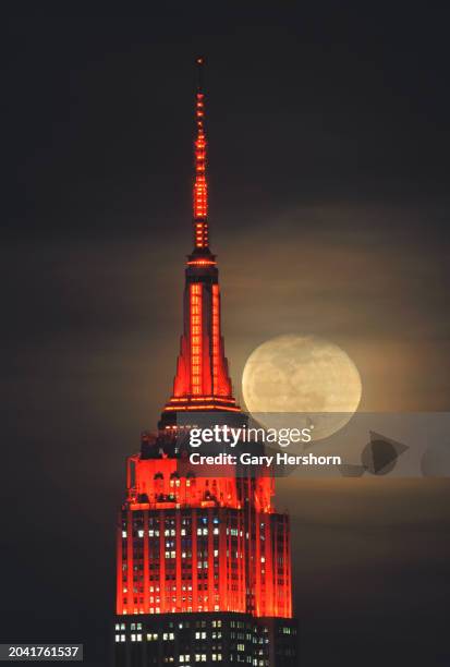 Percent illuminated wanning gibbous moon rises through clouds behind the Empire State Building in New York City, lit in red to mark the 25th...