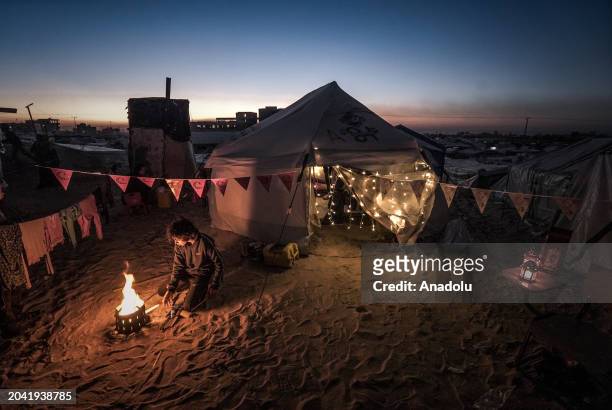 Palestinian boy lights a fire in front of a tent decorated illuminate lights by Palestinians taking refuge in Tel al-Sultan region due to Israeli...