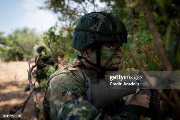 Soldier wearing heavy camoflauge makeup holds a gun in the forest while over 1500 military personnel representing Thailand, the United States of...