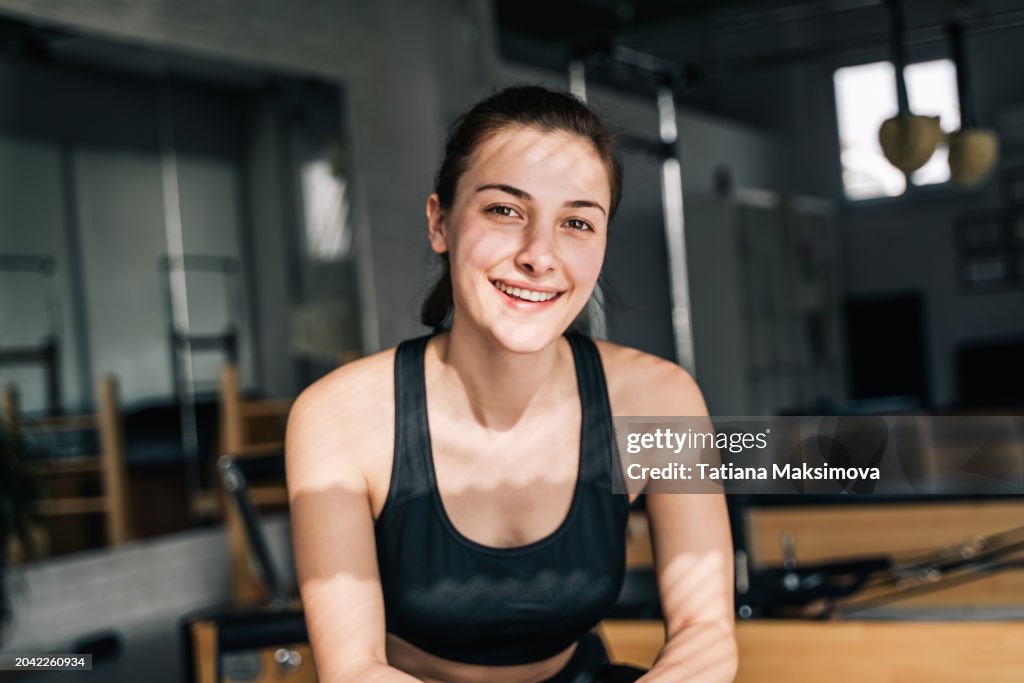 A fitness trainer in the gym on a sunny day, a smiling middle-aged woman in a black tracksuit.