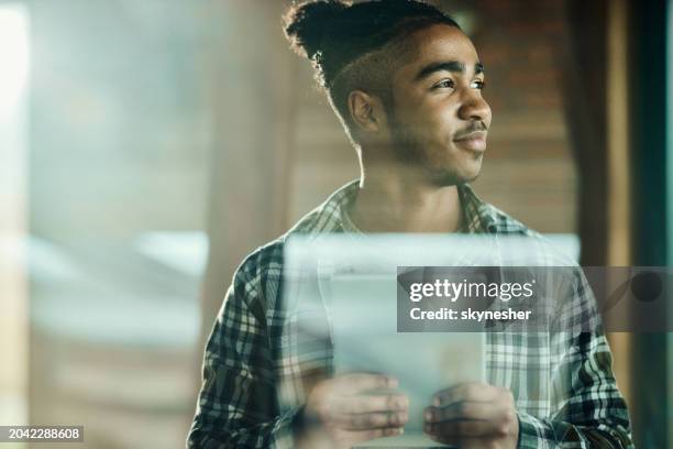 smiling african american man day dreaming while using touchpad. - entrepreneur stockfoto's en -beelden