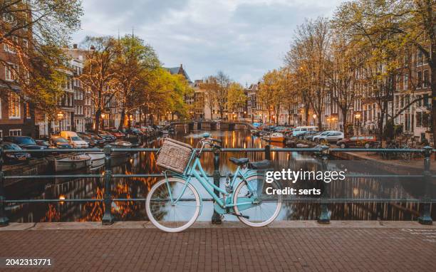 abenddämmerung in amsterdam: blaues fahrrad mit korb auf der grachtenbrücke geparkt - kanal stock-fotos und bilder