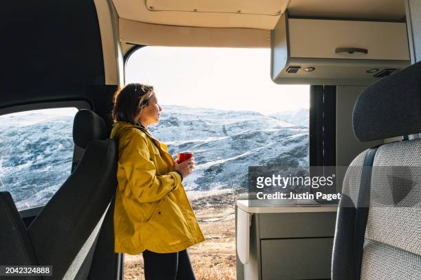 view of a mature woman having a hot drink as she takes in the morning sunny vista of the snowy mountains in the scottish highlands from her campervan - ground culinary stock pictures, royalty-free photos & images