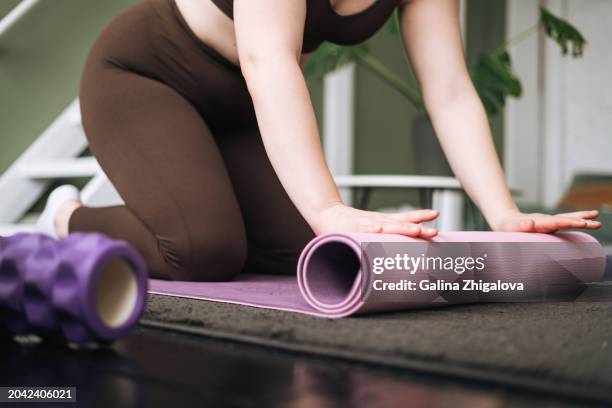young woman plus size rolls out yoga mat in room at home - rolled up yoga mat stock pictures, royalty-free photos & images