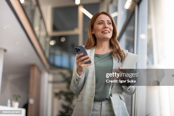 smiling businesswoman using phone in office - ejecutivo fotografías e imágenes de stock
