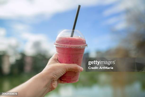 fruit smoothy in plastic take away cup in a woman's hand over city and park background - disposable cup stock pictures, royalty-free photos & images