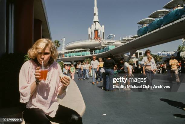 Austrian actress Barbara May, wearing a pale pink peasant top, enjoys a drink and a sandwich, with the PeopleMover attraction in the background, in...