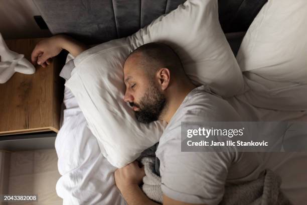 top view apartment bedroom: handsome young man sleeping cozily on a bed in his bedroom in the morning. comfortable apartment with guy resting for productive next day. top down above stock photo - slapen stockfoto's en -beelden