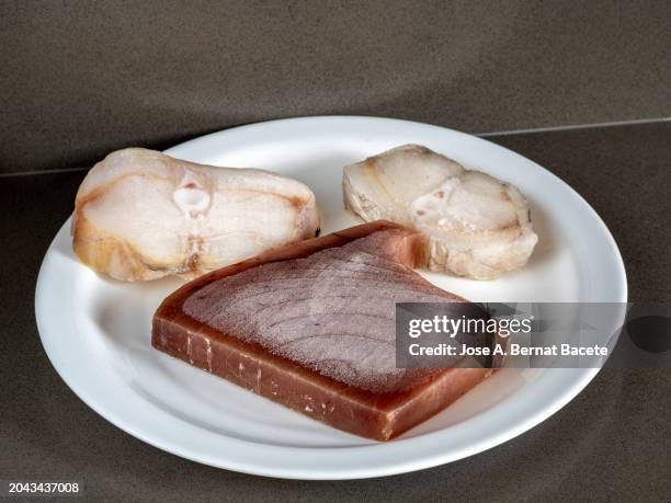 frozen hake and tuna fillets on a plate, thawed in the kitchen to prepare food. - frozen fish fillets stockfoto's en -beelden