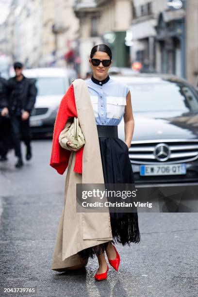 Gili Biegun wears blue sleeveless blouse, black pleated skirt, trench coat, bag outside Victoria/Tomas during the Womenswear Fall/Winter 2024/2025 as...