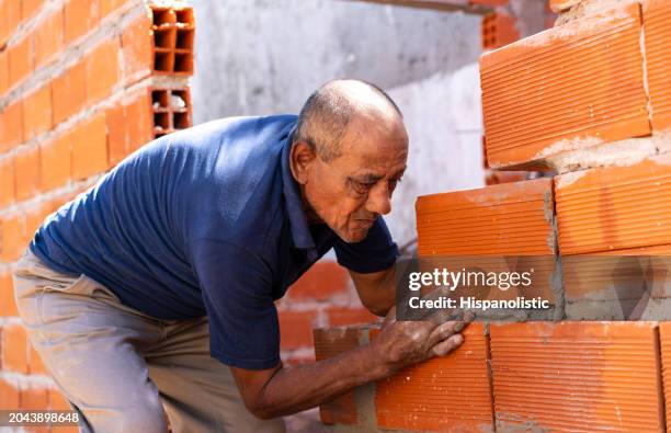 senior man building a brick wall at a construction site - knocked down stock pictures, royalty-free photos & images