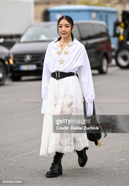 Yuwei Zhangzou is seen wearing a white Dior oversized button down shirt, cream lace sheer Dior skirt, black and silver buckle belt, black and gold...
