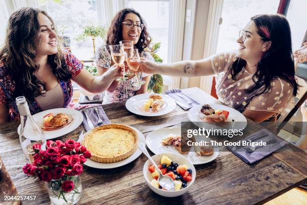 smiling young friends toasting wine while sitting at dining table - brunch stock pictures, royalty-free photos & images