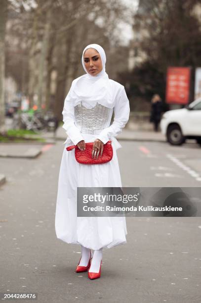 Fatema Alawadhi wears white dress, silver corset, white hijab, white tights, red shoes and red bag outside Dawei during the Womenswear Fall/Winter...