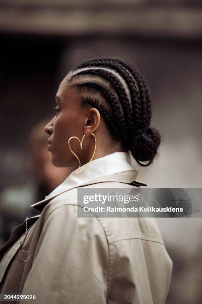 Guest wears cornrow braids, white shirt and beige trench coat and a heart shape statement earring outside Victoria/Tomas during the Womenswear...