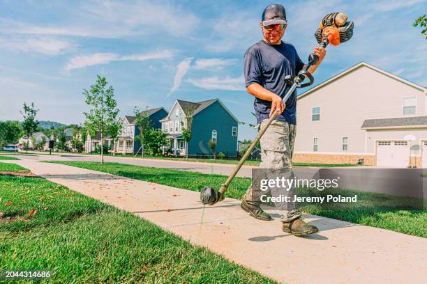 homme joyeux utilisant une tondeuse le long d’un trottoir pour un parc de quartier - terrain paysagé photos et images de collection