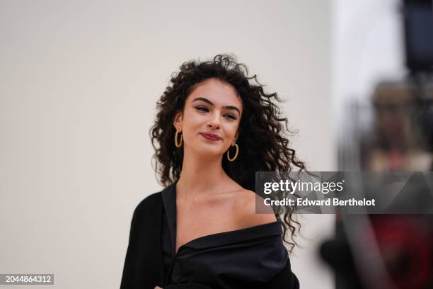 Deva Cassel wears earrings, a black coat, a black asymmetric gathered top, lipstick , outside Dior, during the Womenswear Fall/Winter 2024/2025 as...