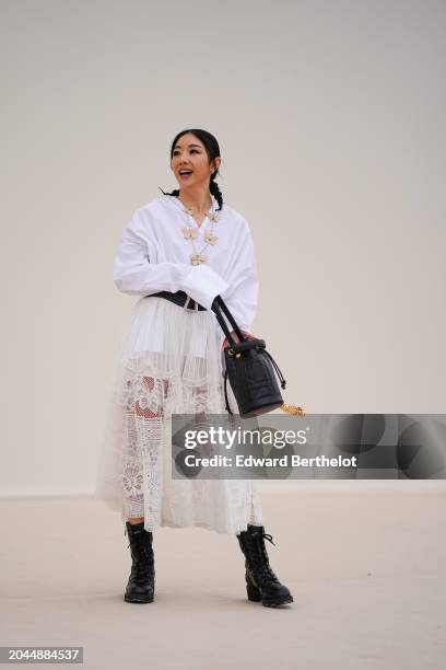 Yuwei Zhangzou wears a white shirt, a necklace with butterfly details, a large belt, a pleated mesh floral embroidery skirt , a black bag, leather...