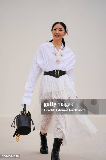 Yuwei Zhangzou wears a white shirt, a necklace with butterfly details, a large belt, a pleated mesh floral embroidery skirt , a black bag, leather...