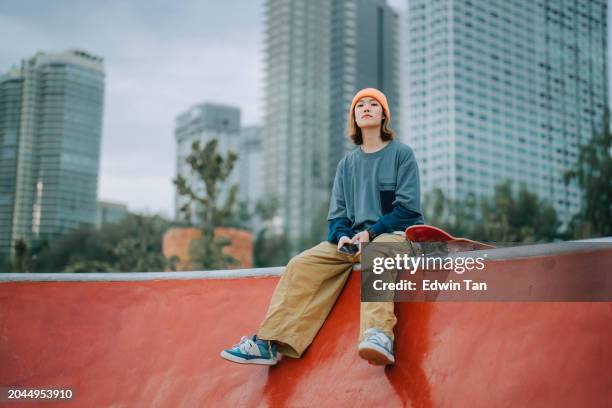 asian chinese female skateboarder sitting at skateboard park looking away - city life authentic stock pictures, royalty-free photos & images