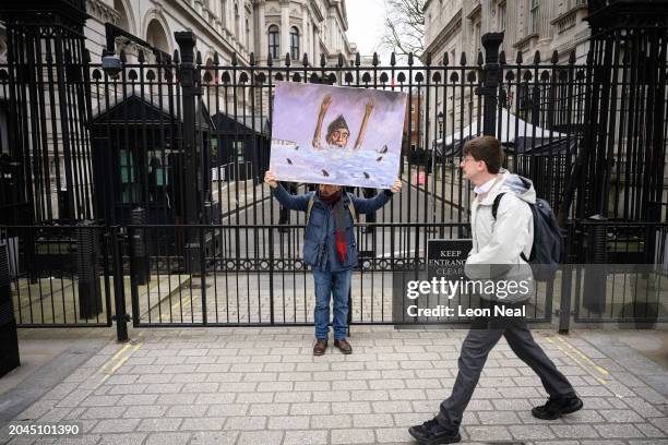 Satirical artist Kaya Mar poses with a painting depicting Britain's Prime Minister Rishi Sunak surrounded by sharks, as he stands outside Downing...