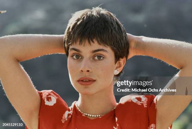 German actress and model Nastassja Kinski, wearing a red top, with heart-shaped earrings, her hands behind her head, United States, December 1980.
