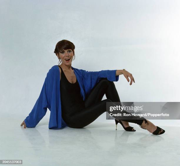 Studio portrait of English actress Judy Carne posed wearing a leotard and leggings under a blue top, London, circa 1975.