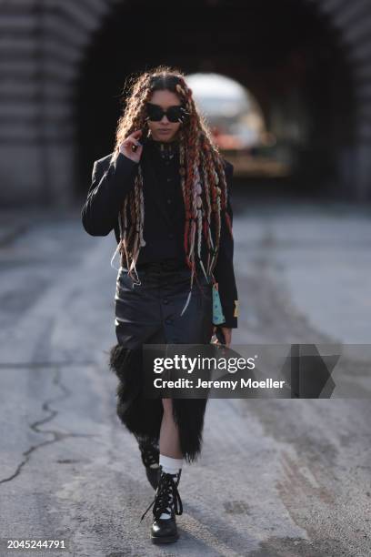 Guest wears black sunglasses with silver studs, black wool knit cardigan, black oversized blazer jacket, black leather buttoned long skirt with black...