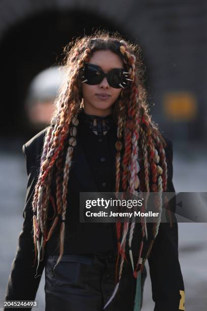 Guest wears black sunglasses with silver studs, black wool knit cardigan, black oversized blazer jacket, black leather buttoned long skirt with black...