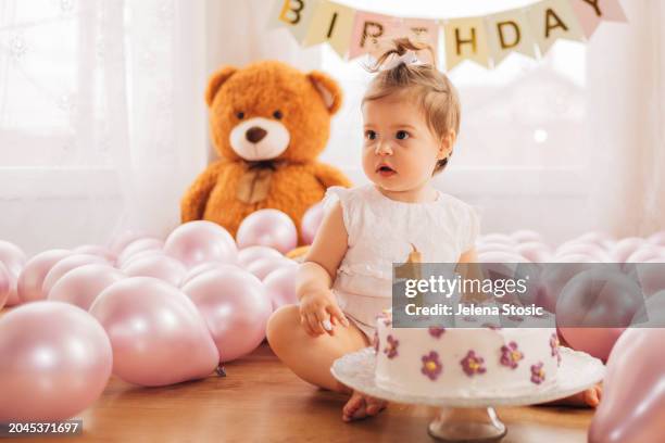 das entzückende kleine mädchen sitzt auf dem boden und weiß nicht, was sie mit ihrem kuchen zum 1. geburtstag anfangen soll. - ein weibliches baby allein stock-fotos und bilder